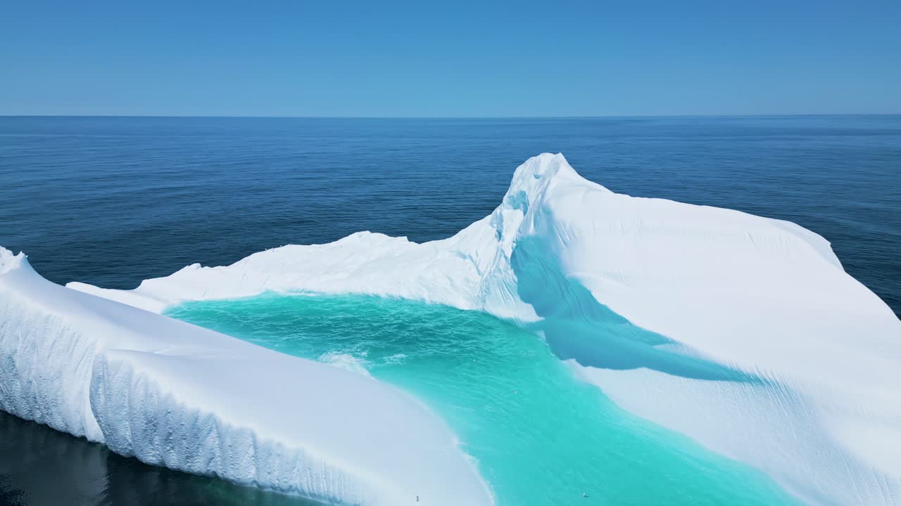 Aerial footage of a large iceberg off Flatrock, Newfoundland, featuring vivid turquoise meltwater in calm Atlantic waters.