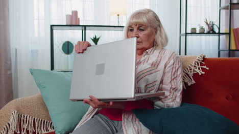abuela mayor mujer usando computadora portátil, escribiendo en la habitación de casa, mirando a la cámara, sonriendo