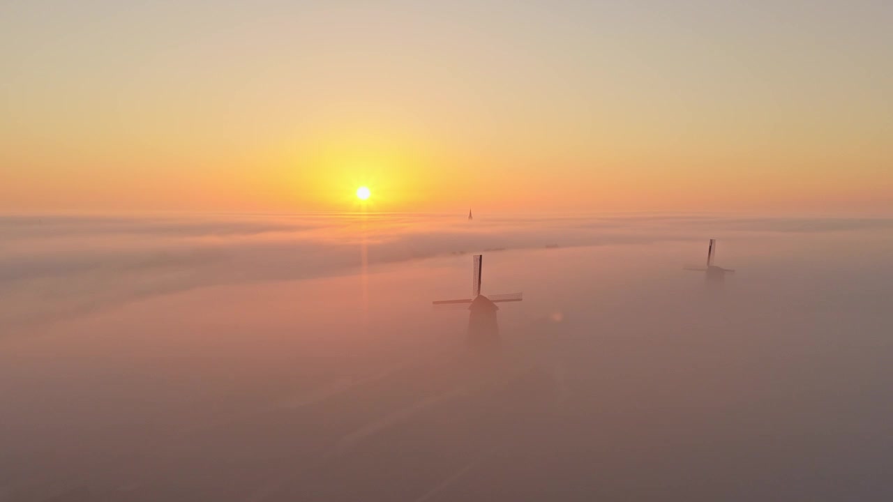 Splendida vista aerea di tradizionali mulini a vento olandesi che si ergono sopra un mare di fitta nebbia durante una splendida e colorata alba in Olanda.