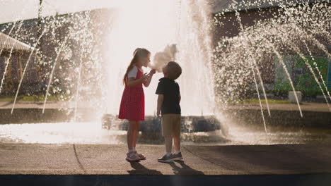 little boy and girl bite candy floss standing by fountain