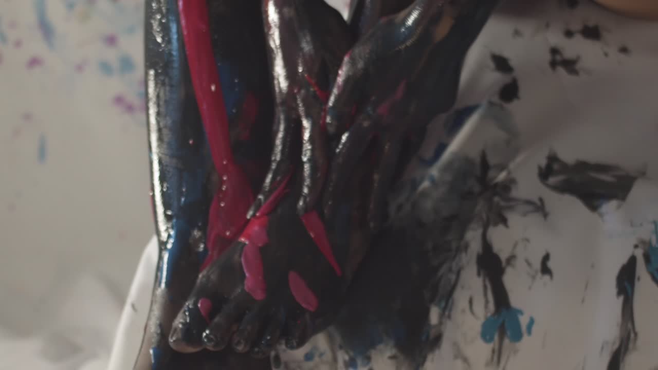 Handheld close-up of girl&rsquo;s hands touching her legs covered in paint