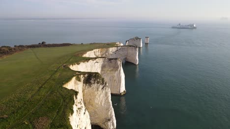 aerial forward along coastal edge of old harry rocks cliffs and boat in background, county dorset in england