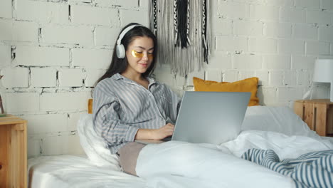 woman working on laptop in bed with eye mask and headphones