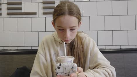 una adolescente en un restaurante de comida rápida bebiendo y mirando su teléfono inteligente