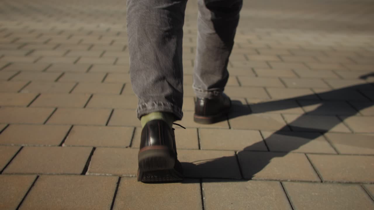 A man is seen ascending concrete stairs, with long shadows from sunlight on a striped pattern cast on the steps