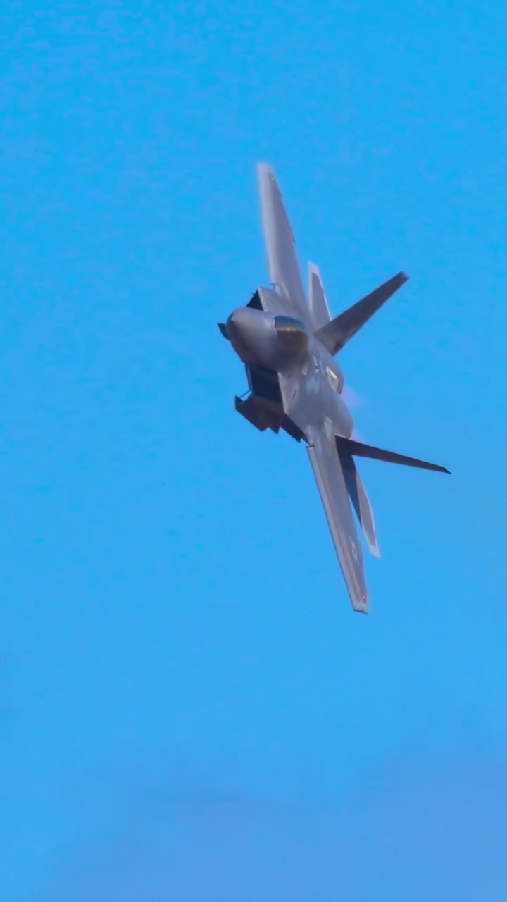 Un moderno jet militare esegue virate e avvitamenti dinamici contro uno sfondo di cielo azzurro limpido.