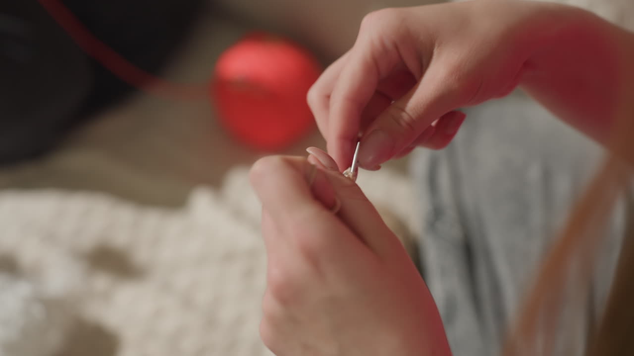 Creación de lana gruesa con intrincados movimientos de los dedos, primer plano de unas manos creando una manta de lana gruesa en el interior, vista detallada de unas manos tejiendo metódicamente una manta de lana roja y lujosa en el interior.
