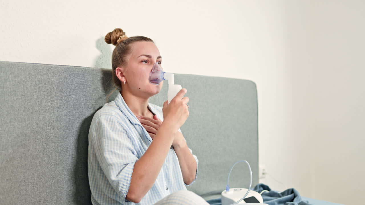 Una mujer trata la tos con inhalación. Mujer enferma en cama con mascarilla nebulizadora realiza inhalaciones para tratar la tos. Joven usa inhalador para tratar el asma. Tratamiento domiciliario de la tos y la neumonía.