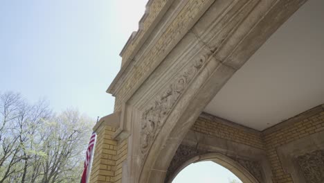 Die-Sonne-Kommt-Hinter-Dem-Verzierten-Torbogen-Aus-Mauerwerk-Hervor,-Im-Hintergrund-Ist-Die-Amerikanische-Flagge-Zu-Sehen