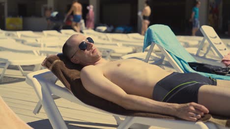 close-up travelling bald married italian man is lying on beach on deck chair sunbathing he is wearing sunglasses