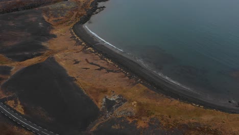vista superior aérea épica sobre la carretera islandesa por la costa de arena negra, olas rompiendo contra la costa, día