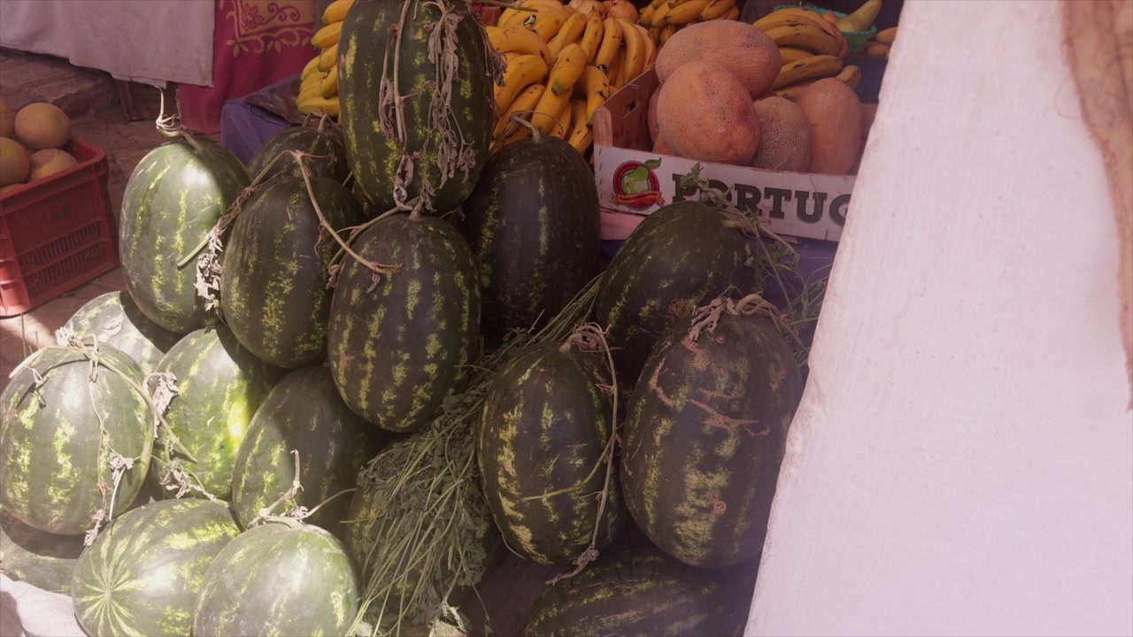Арбузы, сложенные в стопку с бананами и другими продуктами на прилавке открытого рынка.