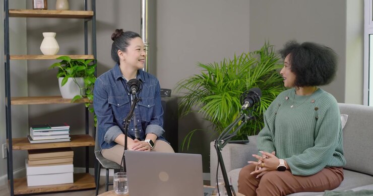 Female host and guest arriving, shaking hands, sitting in studio with microphones for recording