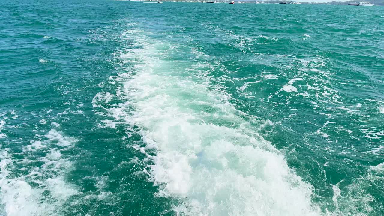 A boat travels through turquoise waters near Phuket, Thailand, under clear skies, creating a dynamic wake