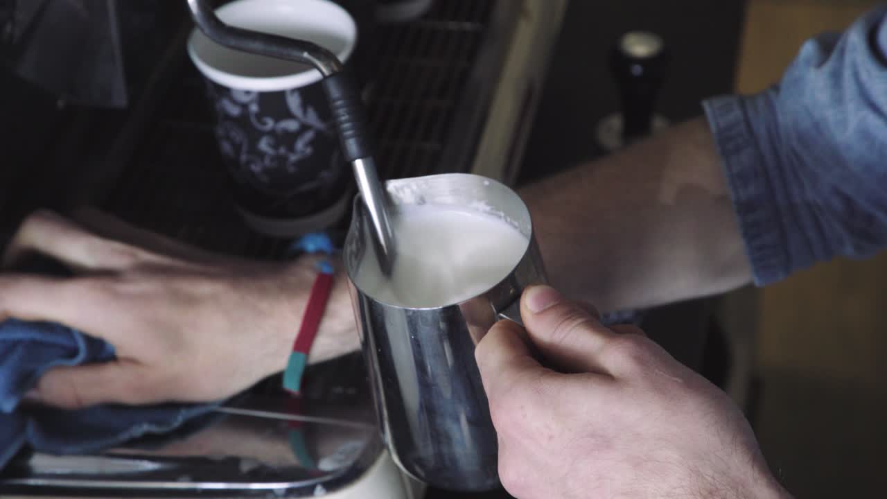 Frothing and heating milk in metal jug next to coffee machine, no steam