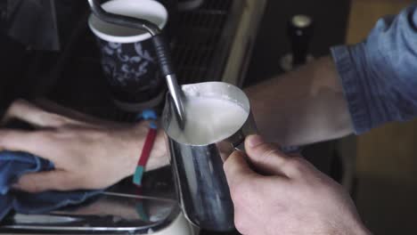 frothing and heating milk in metal jug next to coffee machine, no steam