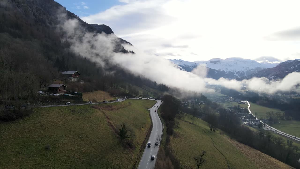 tráfico ocupado en una carretera de montaña mientras la gente conduce para sus vacaciones de esquí con montañas nevadas y nubes bajas en el fondo