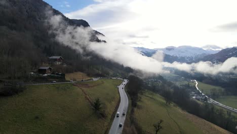 Busy-traffic-on-a-mountain-road-as-people-drive-for-their-skiing-holiday-with-snowy-mountains-and-low-clouds-in-the-background