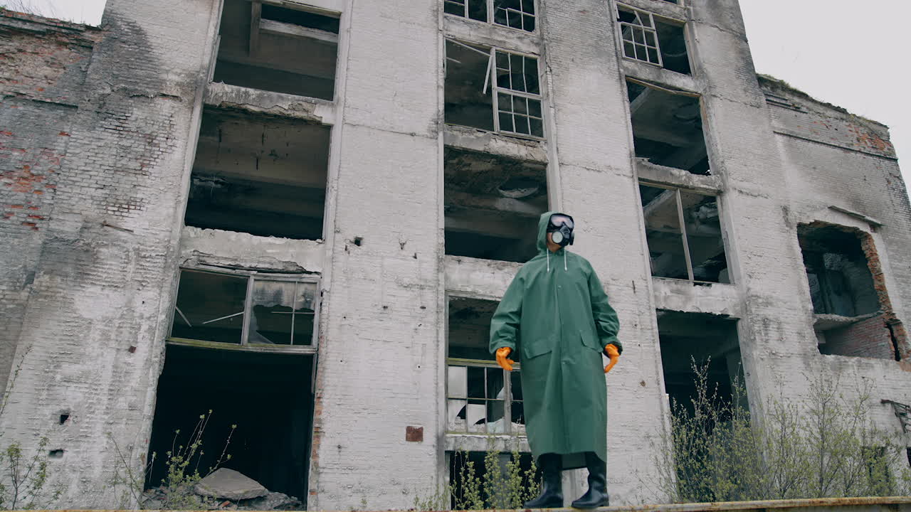 Lab technician in a mask and chemical protective suit walking on dry ground and looking around while thinking about pollution. Ecological catastrophe concept