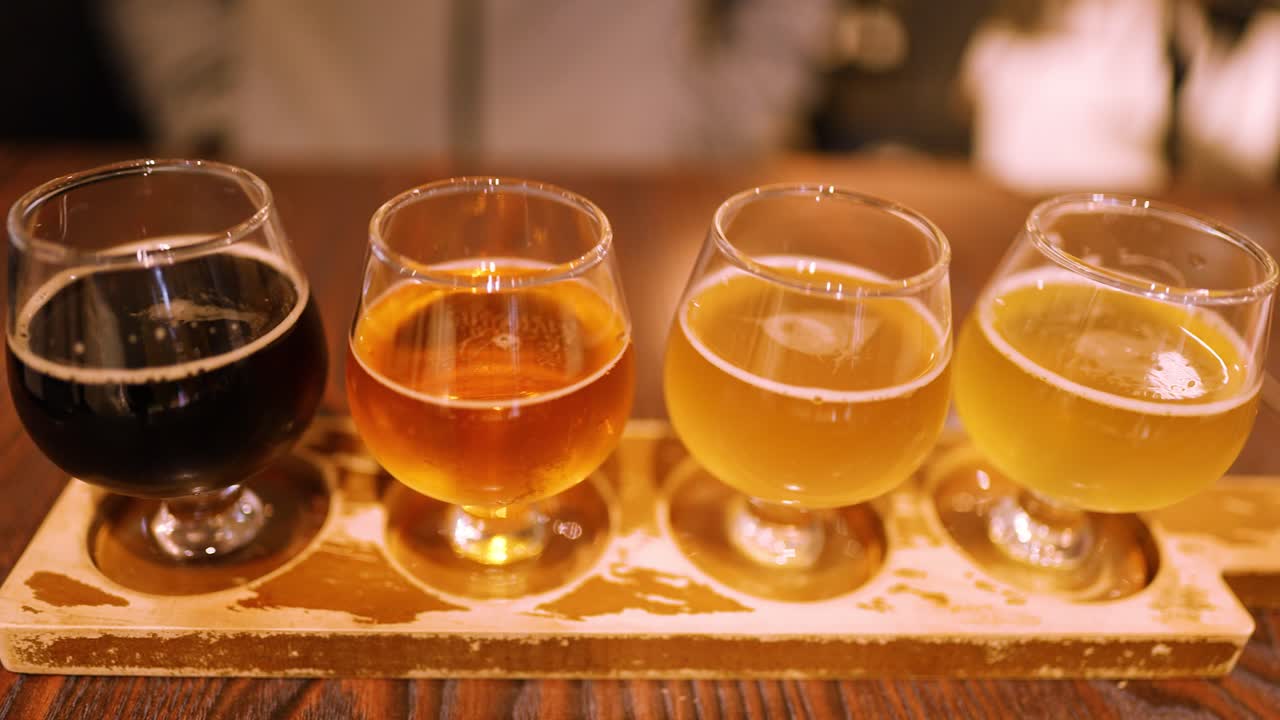 Gros plan de quatre bières artisanales différentes sur une planche en bois sous un éclairage chaleureux