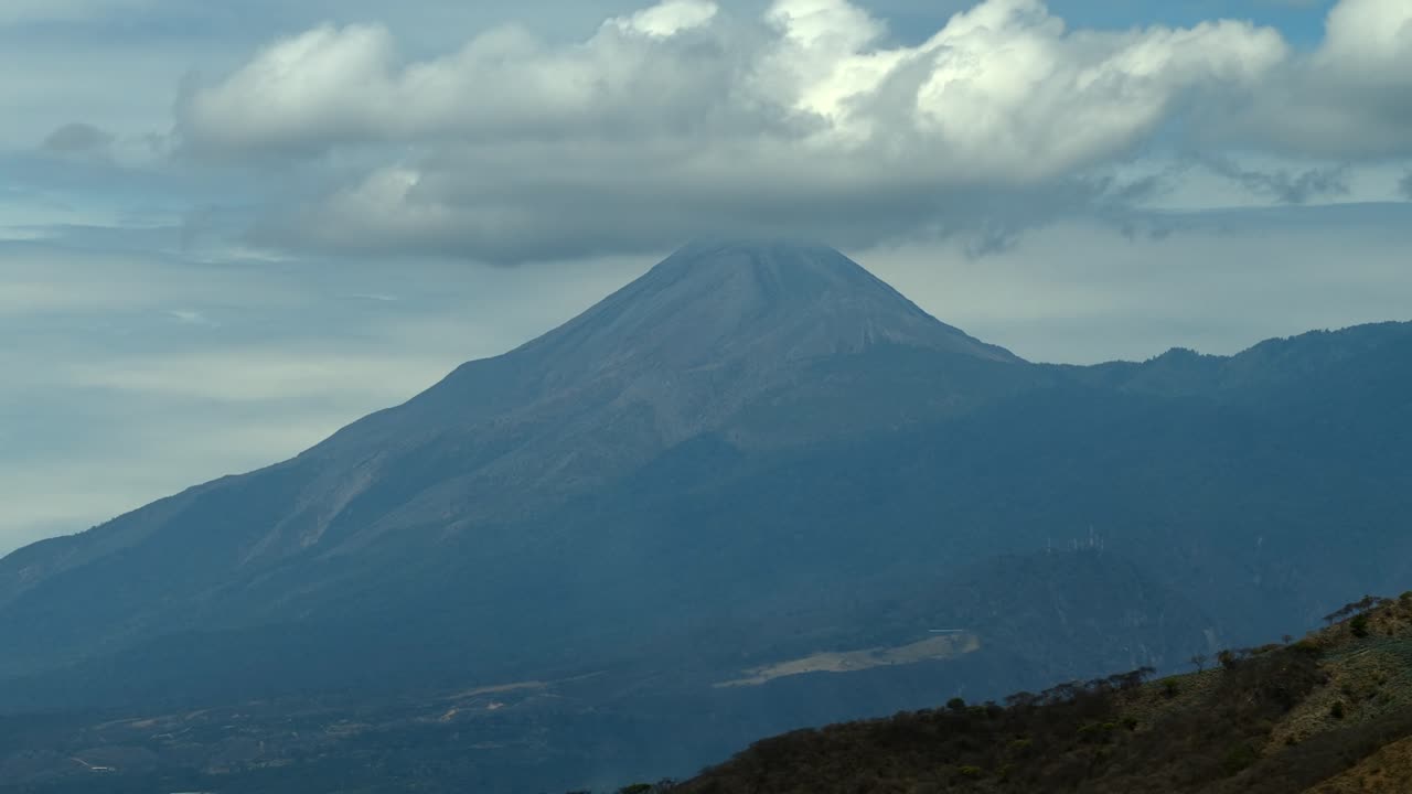 Majestic Colima Volcano with its symmetrical cone and forested lower slopes beneath a cloudy sky near the Jalisco Colima border. Slow drone motion aerial