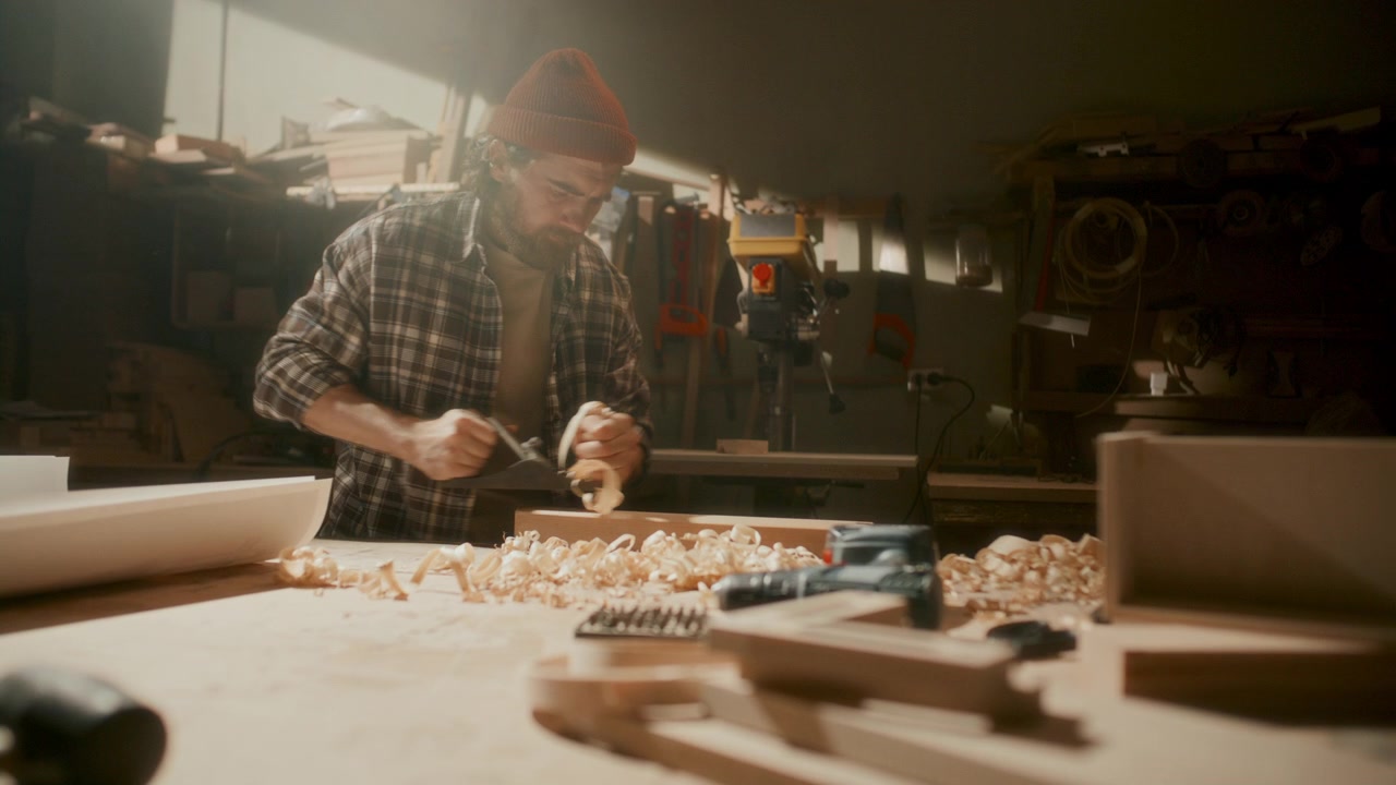 Craftsman Working with Hand Plane on Wooden Board in Carpentry Workshop