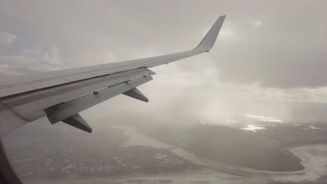 Flying-Airplane-Though-Clouds-View-of-Beach-and-City