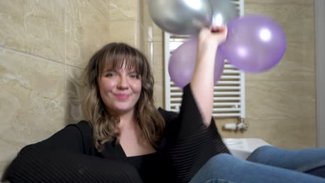 mujer joven sentada en la bañera tirando globos en el baño