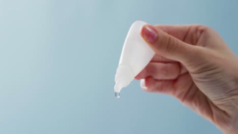 video of hand of caucasian woman dripping solution from dropper bottle, with blue copy space