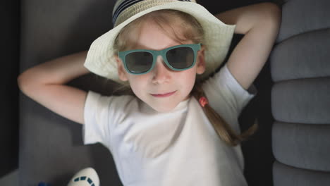 little girl in hat and stylish sunglasses looks in camera