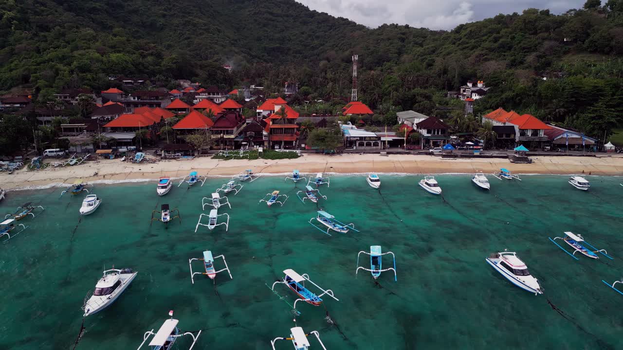 Captured from above, this aerial footage reveals rows of anchored boats floating on clear blue waters in Padang Bai Beach, highlighting the calm tropical atmosphere of eastern Bali