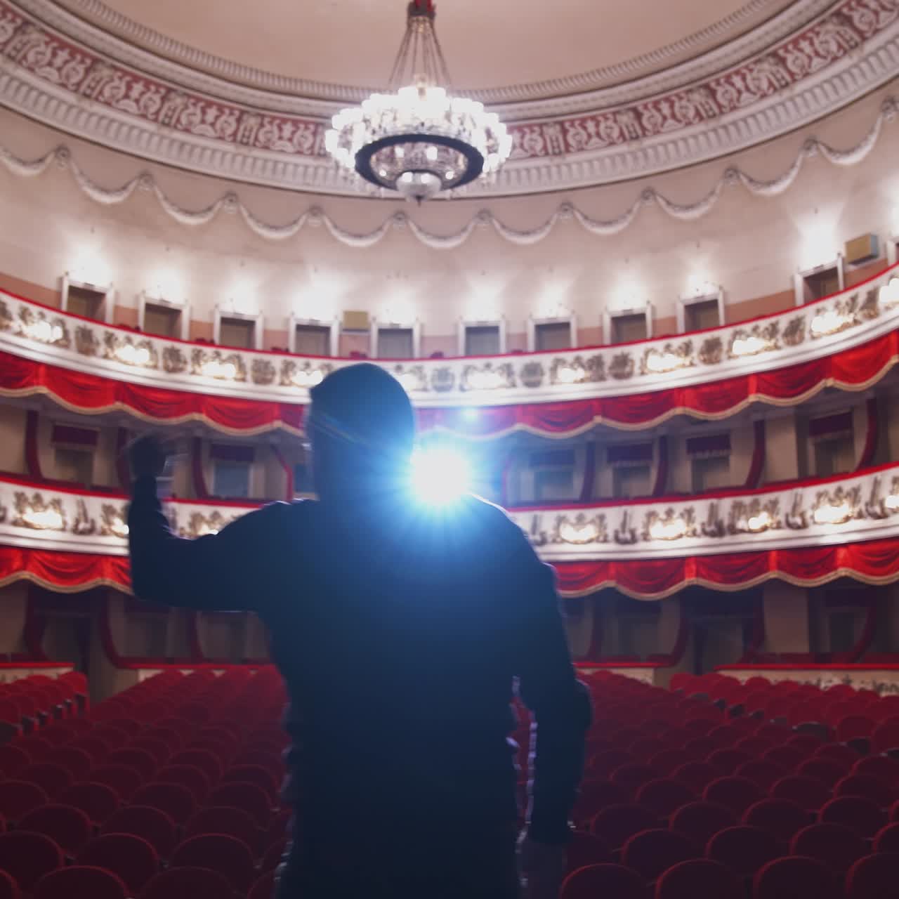 Man on stage in empty theater. Back view of an actor standing on stage and performing in a large theater without people.
