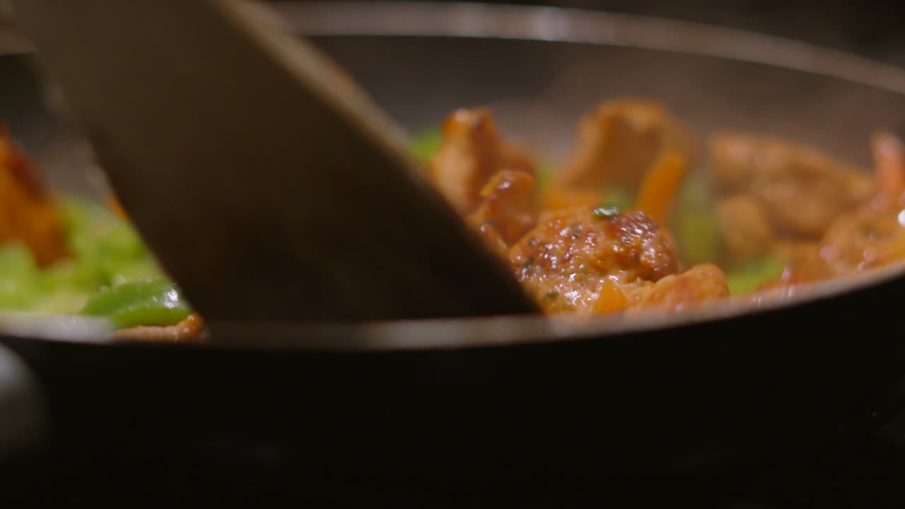 Close Up Side View of Chinese Spice Marinated Chicken Pieces with Vegetables Being Moved Around Hot Pan Cooking For Dinner with Wooden Spatula. Oriental Cuisine Dish 4K.