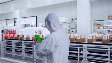 back view of asian male scientist use mock up green screen smartphone while standing with conveyor for packaging coffee beans in bags at coffee factory