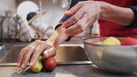 midsection of biracial woman rinsing vegetables in kitchen, slow motion