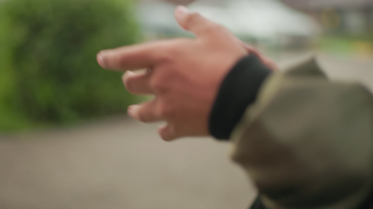 Close up of hands holding handheld device while playing game outdoors, sleeve of jacket visible with blurred background highlighting modern digital interaction in casual urban environment