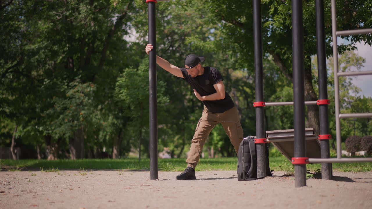 Man Stretches Outdoors, Fitness Instructor Engages In Flexibility Routine In Park Sunlight, Male Fitness Coach Performs Dynamic Stretching Against Pole During Bright Outdoor Training Session