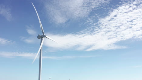 Wind-turbine-spinning-against-blue-sky-in-forested-Swedish-countryside,-aerial