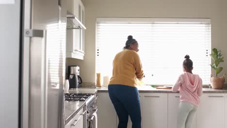happy african american mother and daughter washing up dishes in kitchen, slow motion