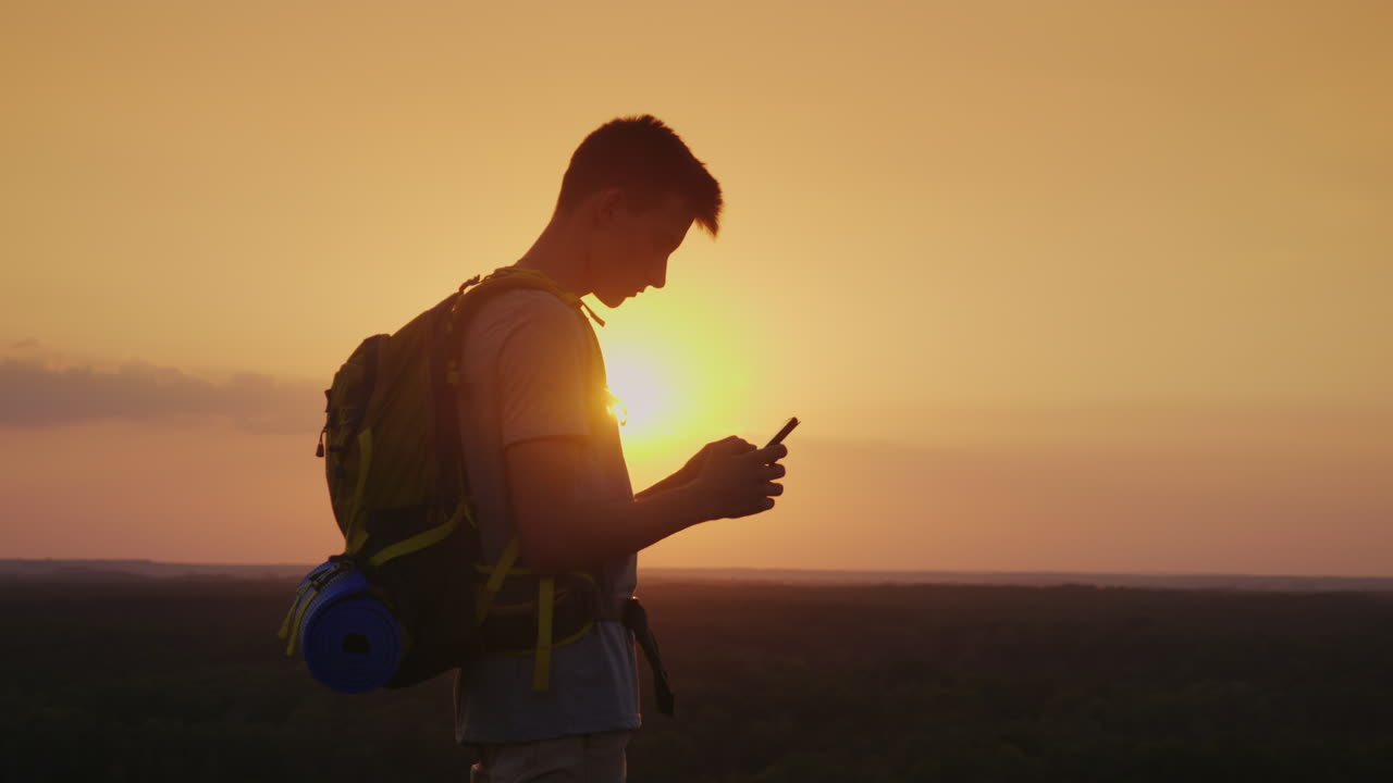Sempre e ovunque connesso, un viaggiatore con uno zaino utilizza uno smartphone. Silhouette al tramonto.