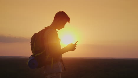 Siempre-Y-En-Todas-Partes-En-Contacto,-Un-Viajero-Con-Una-Mochila-Usa-La-Silueta-De-Un-Teléfono-Inteligente-Al-Atardecer