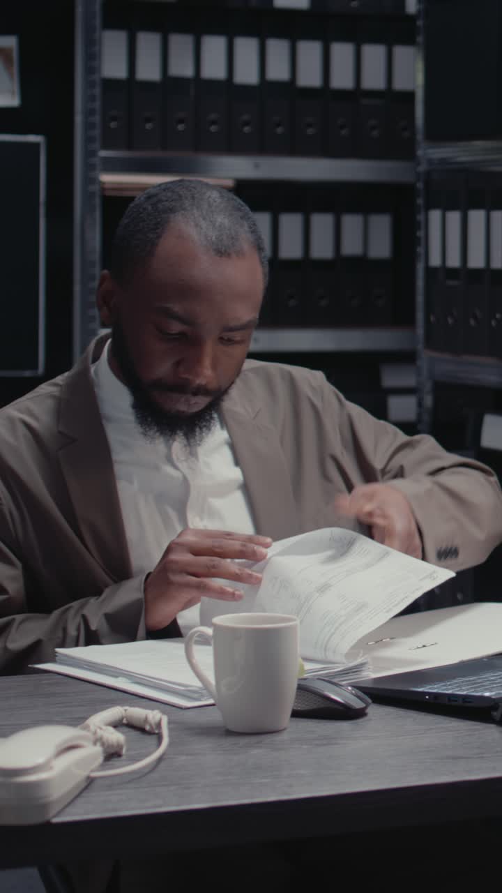 Video verticale: agente afroamericano che legge file sospetti in un archivio