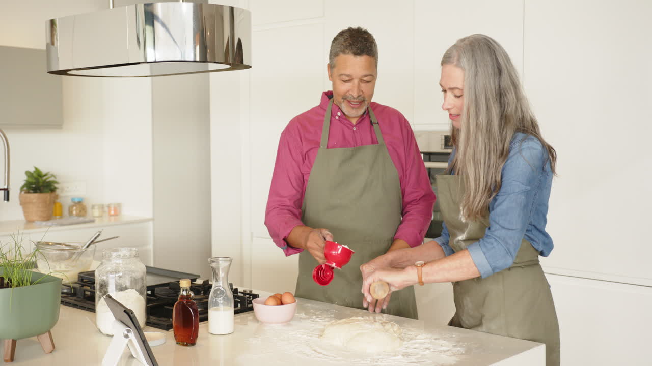 Baking together, multiracial senior couple preparing dough in modern kitchen at home