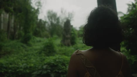 back view of a female traveler looking at a old statue in the middle of trees