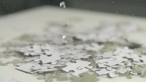 gotas de agua cayendo sobre piezas de rompecabezas blancas y grises colocadas al azar sobre una superficie blanca