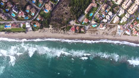 aerial view high up looking down at waves crashing on in on spanish coastline, summer beach view from high in the sky filmed from 4k drone