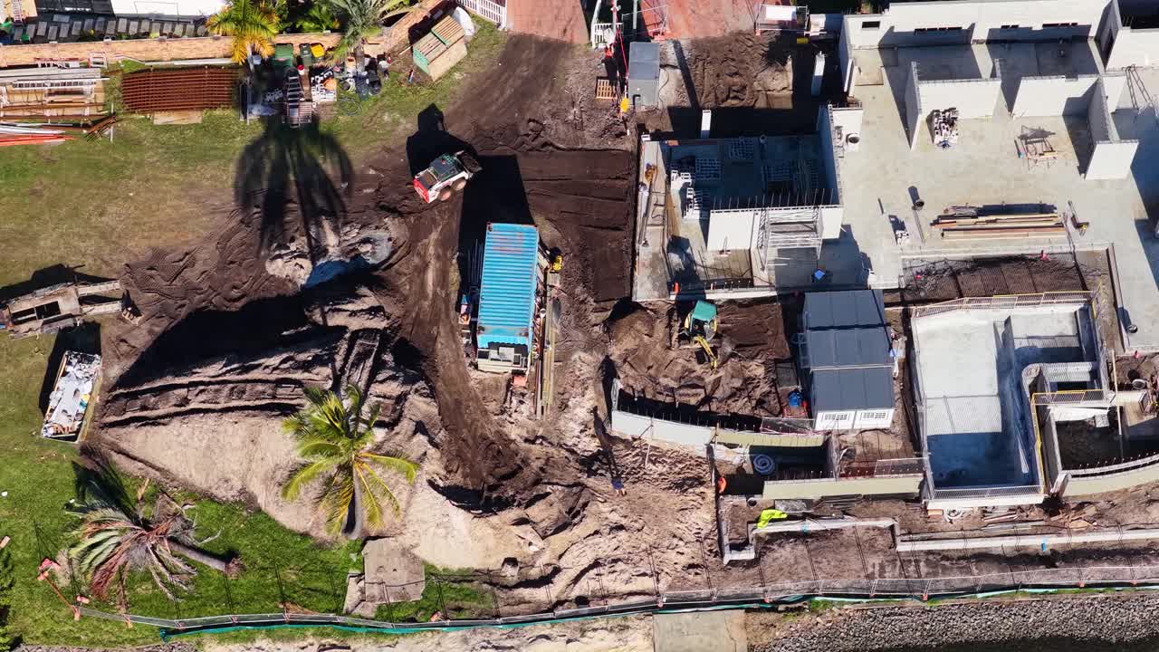 Drone footage captures construction activity near a canal in Gold Coast, Australia, highlighting machinery and workers in a sunny setting