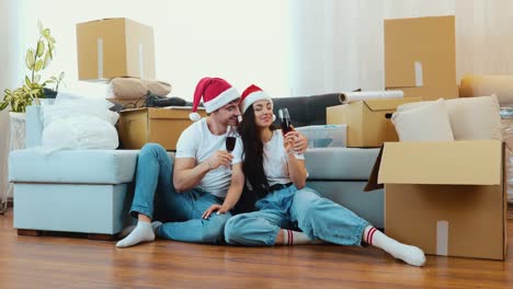 young couple move into new apartment. new year period or christmas time. couple sit on floor and celebrate holidays in new apartment. drink wine and have fun.