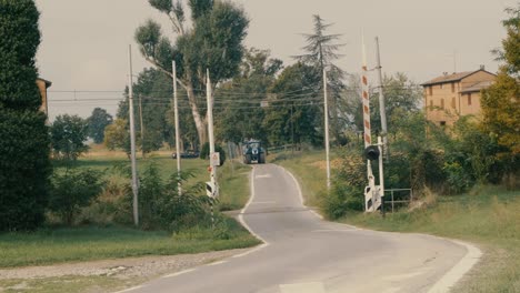 Auf-Einem-Feldweg-Mit-Bahnübergang-Fährt-Ein-Traktor-Mit-Gülleanhänger-Vorbei,-Wir-Sind-In-Der-Poebene-Und-Es-Ist-Ein-Spätsommernachmittag