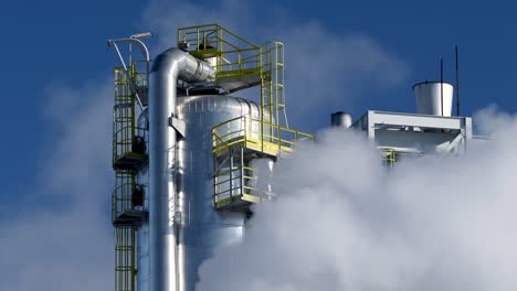 stahltankturm in einer chemieraffinerie, bedeckt von rauch vor dem blauen himmel